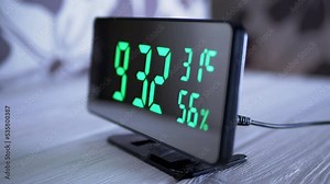 Digital Clock Showing Time on Green Display 9:32 AM, Temperature, Air Humidity. Modern mirror clock, alarm clock with a thermometer, hydrometer standing on a desk on white background. Time concept.