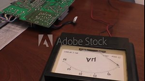 Electronics engineer using old style retro ammeter meter for checking electric current in a circuit on a pcb for a fault