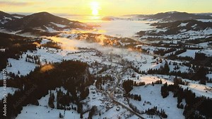 The extraordinary Carpathian valley with snow-capped hills and mountains covered with evergreen spruce forests against the backdrop of a warm bright fiery sunset