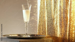 Champagne pouring into a glass on sparkling gold background