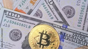 Golden physical coin Bitcoin on banknotes of one hundred dollars rotate. Bitcoin lies surrounded by dollars. Cryptocurrency vs paper money background.