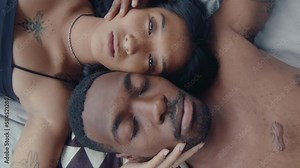 Overhead shot of young loving couple lying down head to head together on bed, gently touching each other, posing on camera