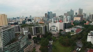 Aerial view of Singapore's cityscape featuring skyscrapers, SMU campus, green spaces, roads with traffic, and a cloudy sky on a bustling day.