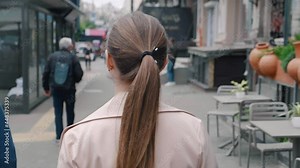 Back view on the caucasian young business woman walking the street in the center of the big city. Outside. Rear view. Slow-motion