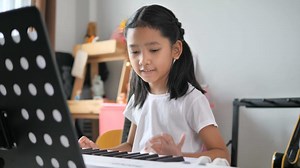 Asian little girl learning to play basic piano by using electric synthesizer keyboard for beginner music instrumental self studying at home