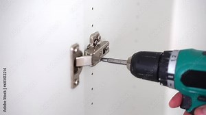 Cabinet hinge installation. Screwing screw with screwdriver on wooden furniture.