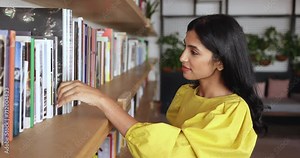 Pretty Indian woman choosing books in public library. Attractive millennial business woman collects information for project or corporate task, search literature, select text-book, working in office