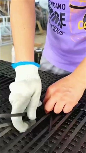 White glove weaving black plastic strips into grid form