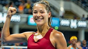 A young tennis player smiles broadly, raising her fist in celebration after winning a match. The excitement of the crowd enhances the electric atmosphere around her.