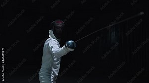 Professional fencer in protective uniform practicing maneuvers with sword alone in dark studio . Fencing demonstration on black smoked background . Shot on Arri Alexa cinema camera in slow motion .