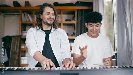 Friendly male instructor teaching a smiling teenage boy how to play a song on an electronic keyboard. Private music class at home