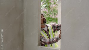 Indian architect with mustache uses water level measuring device. Intended to check slope of a concrete wall. and window sill Man wearing green reflective vest and safety helmet at construction site