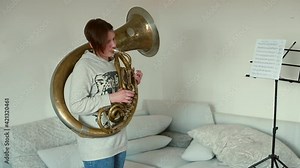 Girl teenager prepares to play the Helicon. She stands in front of the notes, begins to play the melody. Learning music in self-isolation. Camera movement.