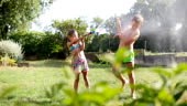 Little kids fooling around in yard in summertime with girl spraying...