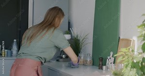 Young woman housewife wiping table doing clean-up and housework in kitchen in apartment. House chores and hygiene routine concept.