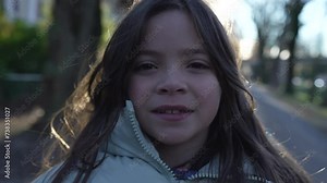 Close-up face of 8 year old female child looking at camera standing outside during sunset. Portrait of little girl wearing jacket during autumn