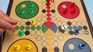 People play Ludo or Pachisi board game on beautiful wooden play board. Ludo is strategy board game for two to four players. 4K resolution family board game video.