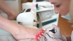 Pedicurist doing white nail polish on client legs using shellac lamp...