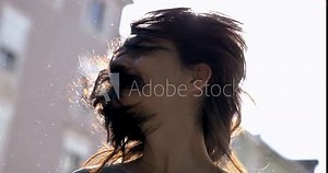Carefree woman shaking hair in super slow-motion outside in the sunlight with flare. 800 fps clip of 30s adult girl shakes head sideways