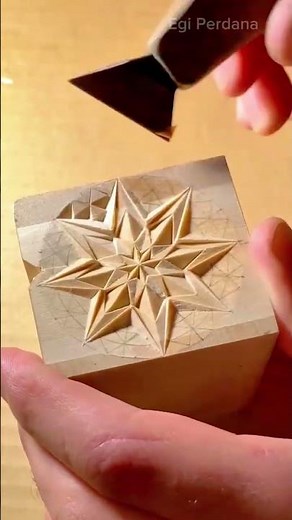 carving a geometric star pattern into a wooden block using a specialized chip carving hand tool