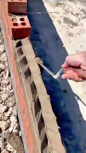 Spreading wet cement mortar over a brick wall and carefully placing new red bricks into a neat row