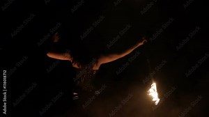 Female fire dance performer dancing with burning fire on black background. Brunette woman juggles with fireballs dance show outdoors