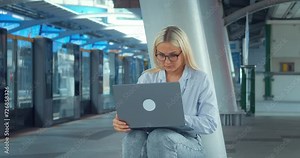 Woman using laptop at subway station metro platform. Young student does homework writes essay finishes project outside of school hours before classes at university. Serious female studying on laptop