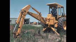 1960s: A backhoe digs a hole in a field.