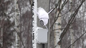 outdoor IP security camera spins rotating follow track watch on a concrete pillar with a power box and LED. Winter with snow. High quality 4k footage