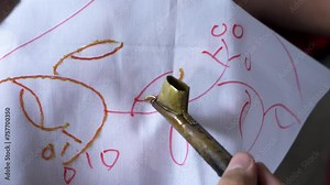 4k footage of participants learning to make traditional batik using hot wax in a pan and canting drawn on a piece of white cloth. The process of beginners learning to paint traditional Javanese batik
