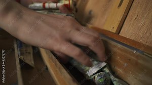 Young artist, designer dismantles working wooden easel painting portraits, landscapes old used tubes paint that he will longer use. Cleaning rubbish, stale inventory. Contemporary fine art NFT culture
