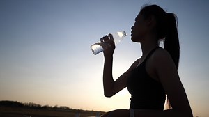 Download Woman holding bottle up to drink water after exercise for free