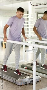 Vertical video: Man in rehabilitation walking on treadmill using parallel bars for support