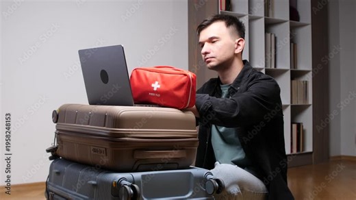 Man packing an essential first aid kit into luggage, ensuring safety and preparedness for an upcoming journey while using a laptop for planning at home