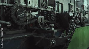 Close up of a powerful chain drive mechanism on an industrial machine, with heavy duty gears and sprockets rotating to power the automated production line inside a factory plant