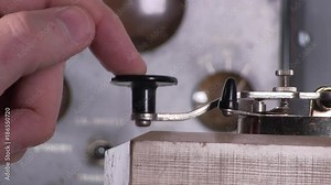 Extreme close-up of finger pressing telegraph key and adjusting to send morse code radio transmission with vintage electronic hardware engineering military lab test equipment device in the background