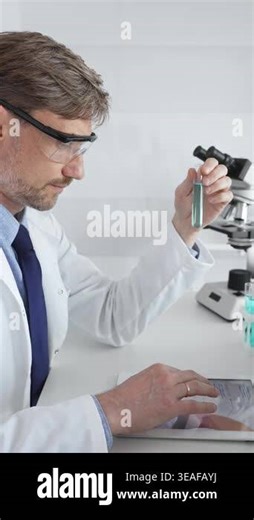 Male adult scientific researcher wearing protective eyewear, holding blue liquid test tube, working on tablet within sterile laboratory environment. Medicine and science concept Stock Video Footage - Alamy