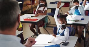 Animation of graduation cap icons over diverse schoolchildren and teacher wearing face masks. education, learning and development during covid 19 pandemic concept digitally generated video.