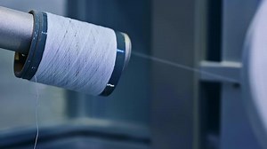 Nylon white thread being unwind from a thick reel. Thread used for sewing the diaper parts at the nappies factory. Close up.