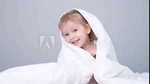 Cute cheerful funny little child in pajamas wakes up in the morning in white bed in bedroom under the blanket again with play peekaboo in blanket. kid sleeping. baby girl playing
