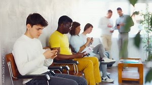 Serious man browsing websites on smartphone while sitting in lobby of job center or employment office, waiting for interview or conversation with career counselor. High quality 4k footage