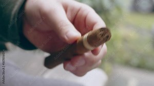 Hispanic man cutting end off fine cigar on front porch