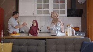 Pregnant woman with Muslim hijab, her husband and their little girls wearing hijab dance with great fun. Muslim family have a good time dancing and singing in the kitchen together.