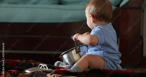Baby playing with kitchen utensils holding pots and pans at home, creative curious toddler infant