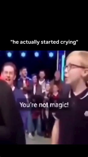 Aqonira on Instagram: "In this video is a staged magic show setting with audience members visible in the background, a young boy in glasses confronts a magician—dressed in a tuxedo with a red-lined cape—accusing him: *“You’re not magic!”* The magician retorts with deadpan sarcasm, *“About as magic as your dad mate,”* followed by, *“He disappeared didn’t he?”*—a darkly humorous jab implying the boy’s father is absent (likely deceased or estranged). The crowd reacts with laughter and shock, while 