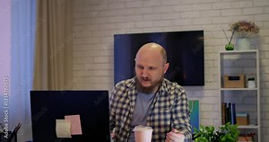 Bald man stares blankly at screen, showing exhaustion creeping into daily routine, where exhaustion diminished morale and exhaustion signals urgent need for self-care. Drinks coffee