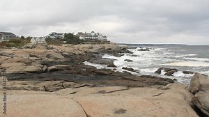 Waves splashing against the rocky coast of the Atlantic Ocean in Maine. Luxury homes seen in the background.