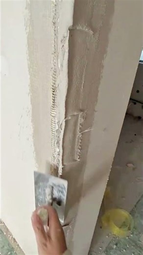 applying a smooth layer of white plaster putty to an interior wall corner to create a flat surface