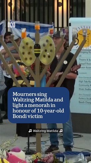 ABC Sydney on Instagram: "Mourners have gathered outside Bondi Pavilion to sing Waltzing Matilda and light a menorah in honour of the 10-year-old Bondi victim. A big bumblebee was placed on the menorah as a nod to Matilda's middle name 🐝 #ABCNewsNSW #ABCNews"