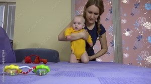 mother make with baby daughter sport exercise train child muscle on sofa. Baby care and motherhood. Static tripod shot. 4K UHD video clip.